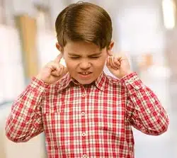 Handsome toddler child with green eyes covering ears ignoring annoying loud noise, plugs ears to avoid hearing sound. Noisy music is a problem. at school corridor